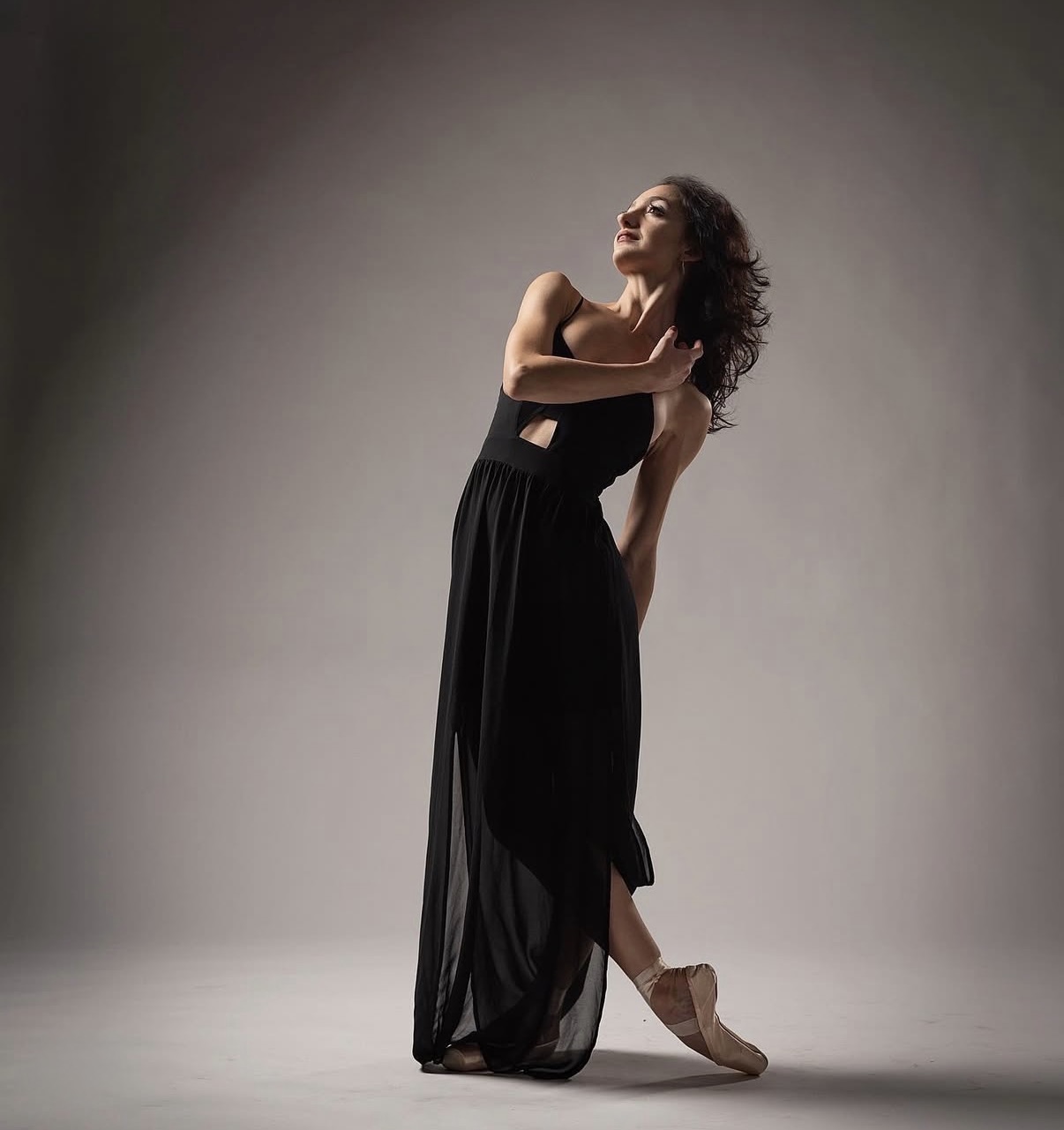 Buse Babadag in black gown, contemporary pose on gray backdrop