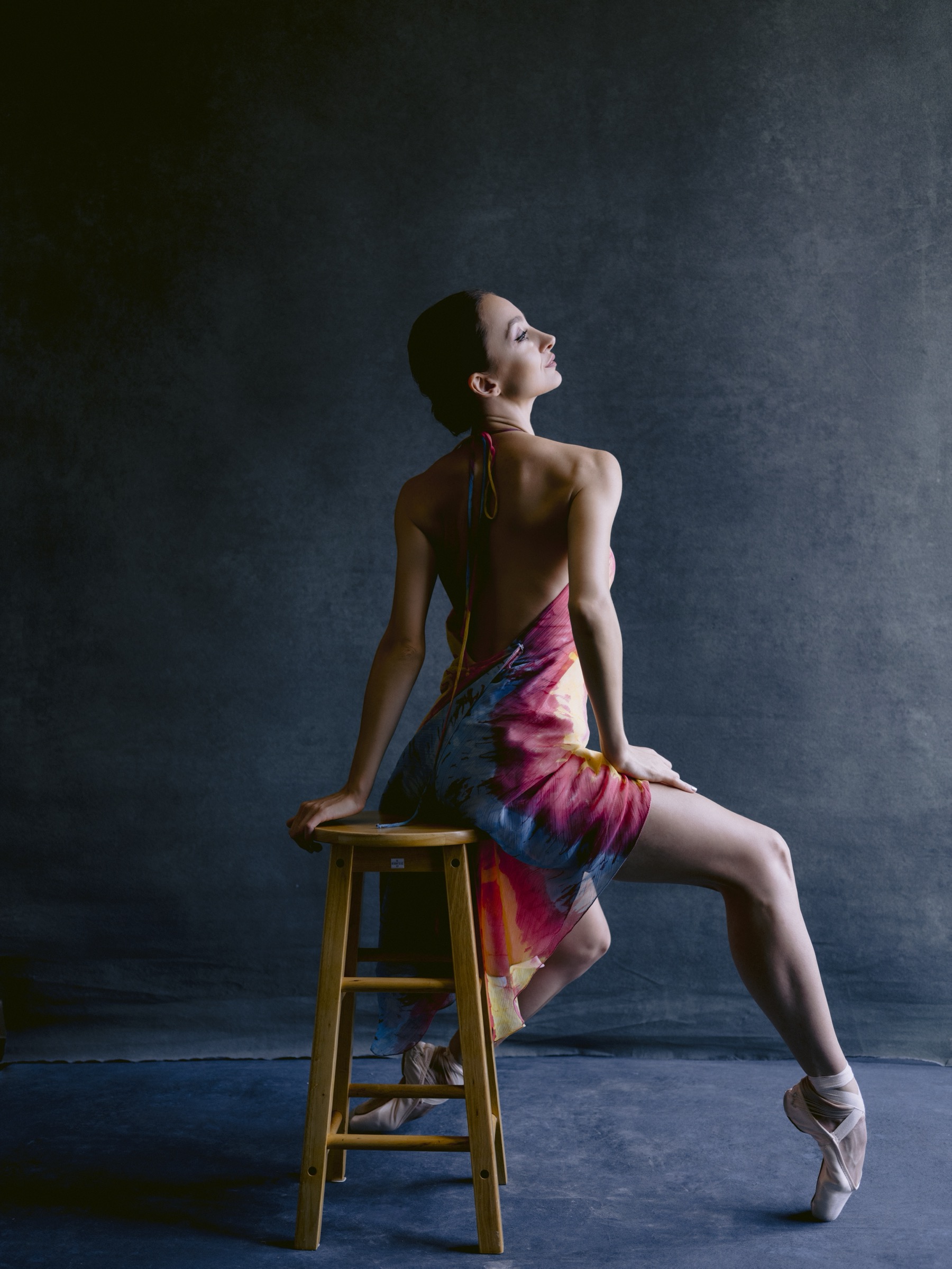 Buse Babadag seated back-to-camera on stool in colorful dress, en pointe
